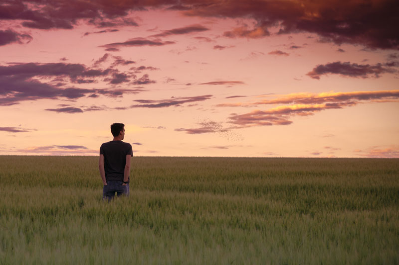 Man standing in grassy field, looking toward the horizon